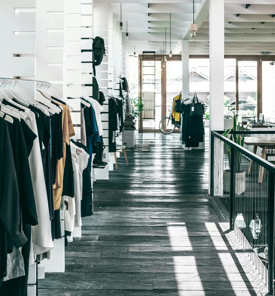 Interior of spacious modern fashion boutique with collection of various clothes hanging on racks in sunlight